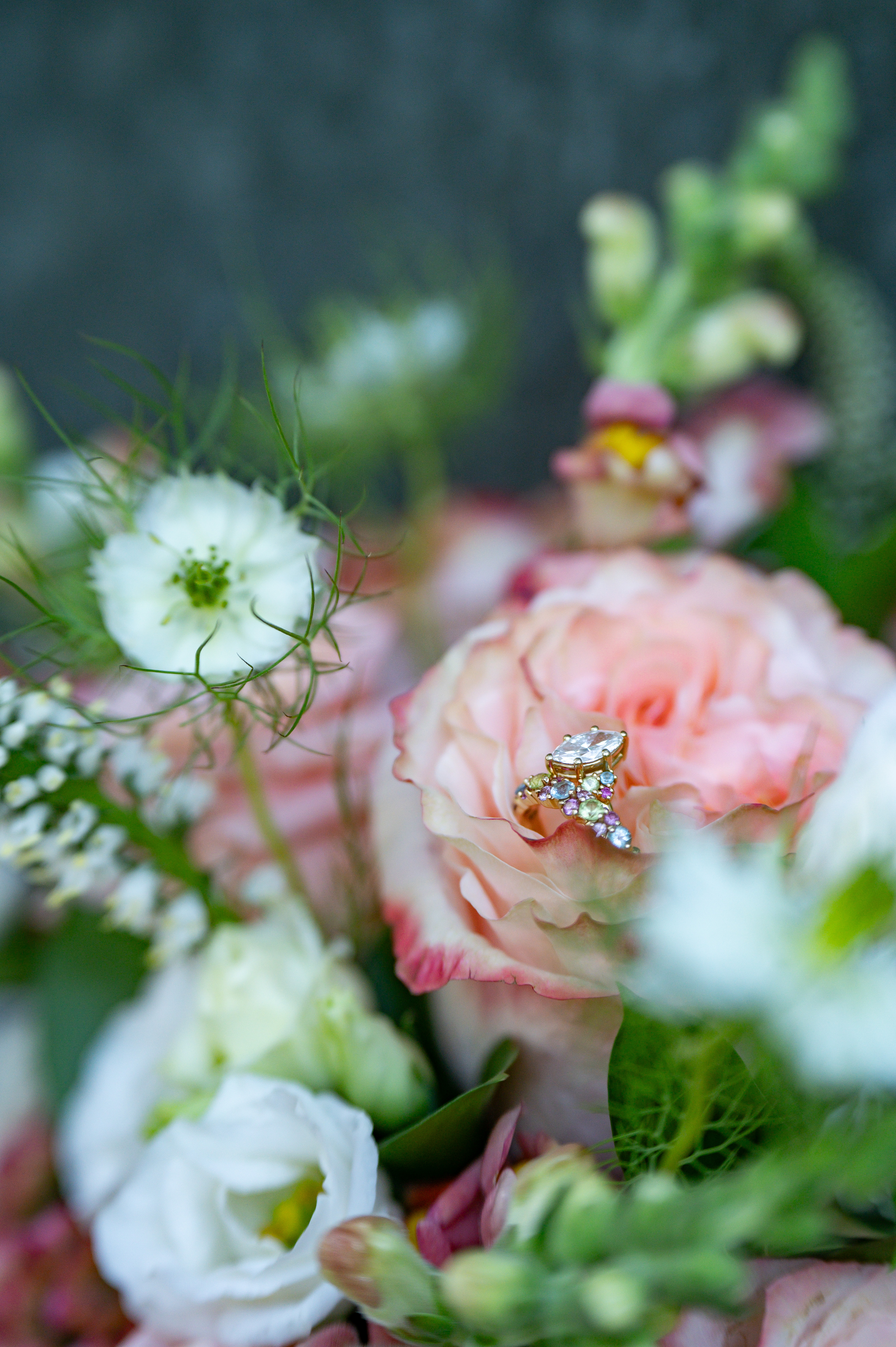 A ring with a large centre stone and pastel side stones, resting on a peach garden rose.